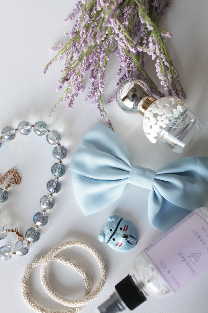 Flat lay of lavender, bow, jewelry, and perfume creating an elegant arrangement on a white background.